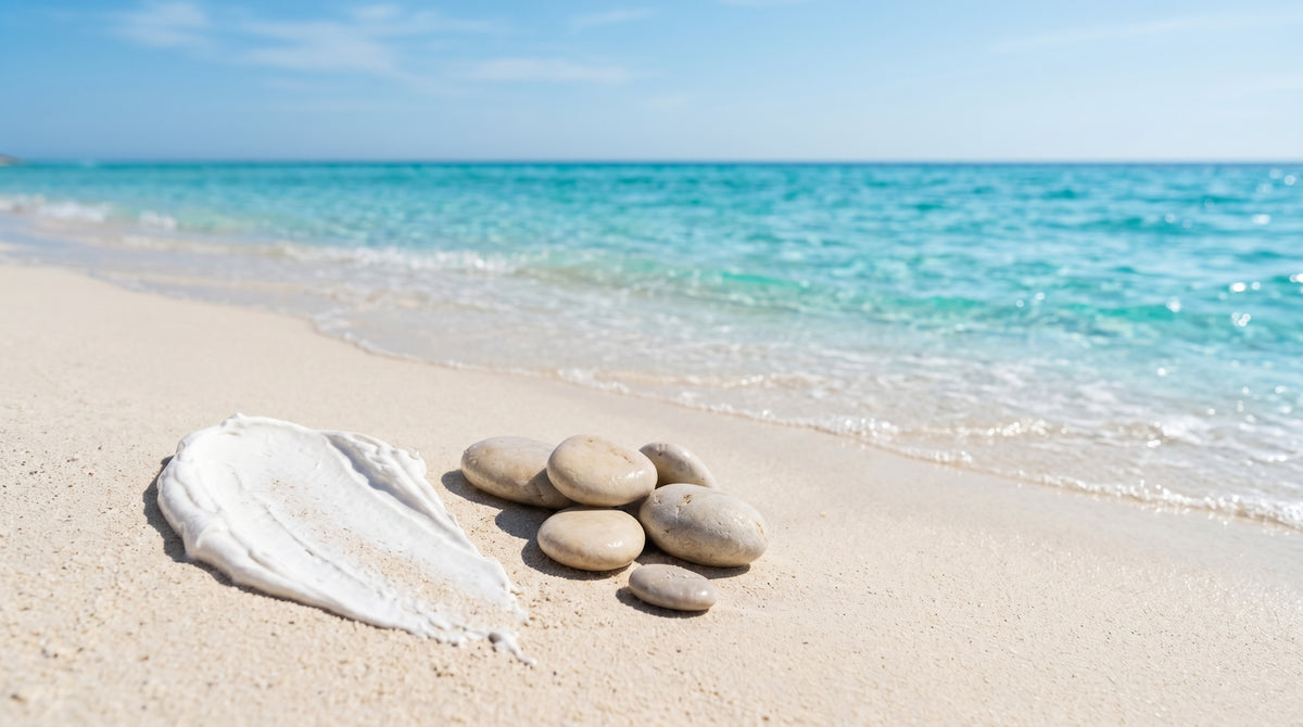 Mineral sunscreen cream and pebbles beside clear turquoise ocean water