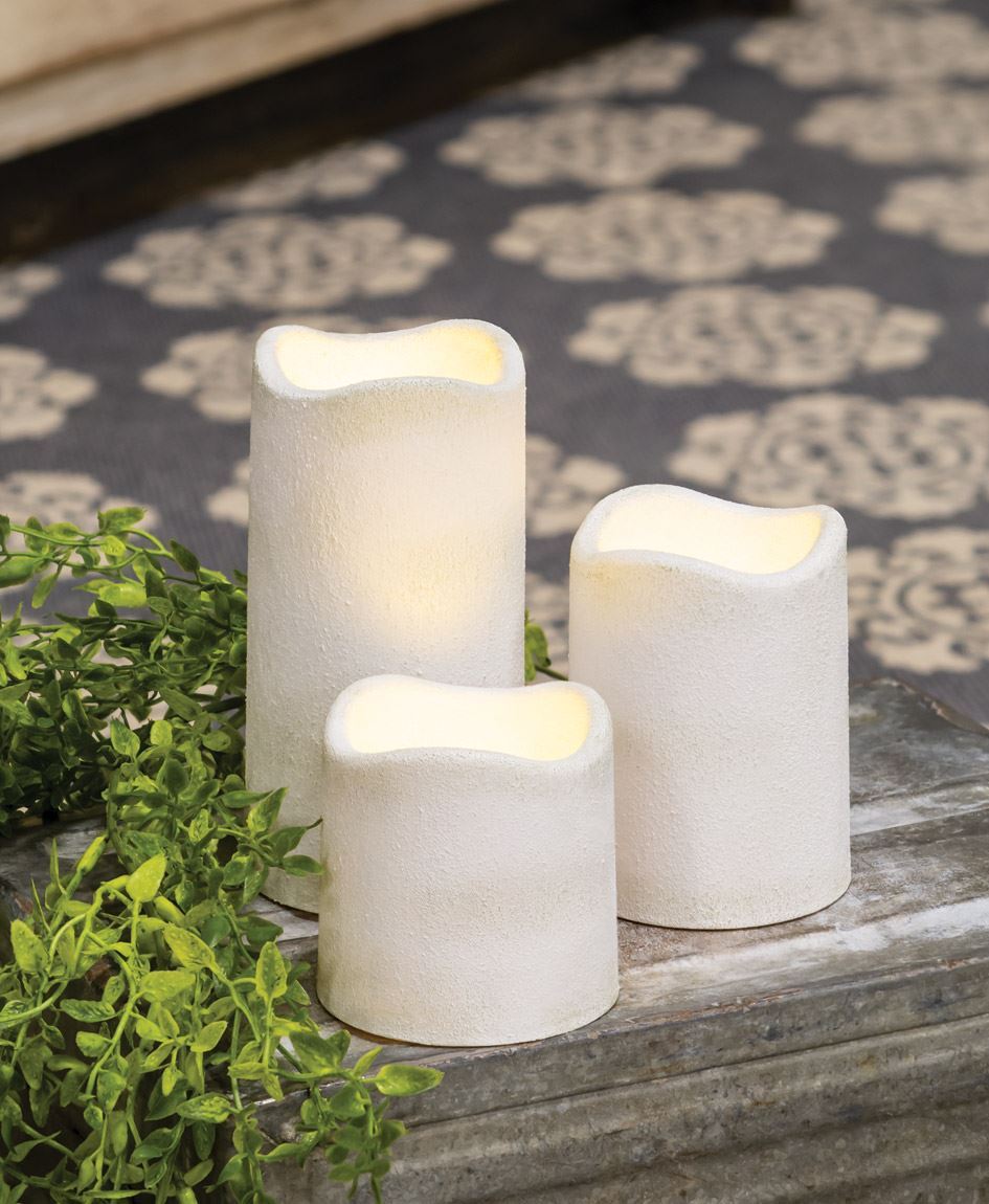 Set of three white textured pillar candles with battery-operated flickering light on a rustic surface.