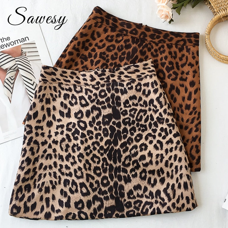 Two high-waisted A-line mini skirts with brown and tan leopard print, displayed folded on a white surface next to flowers.