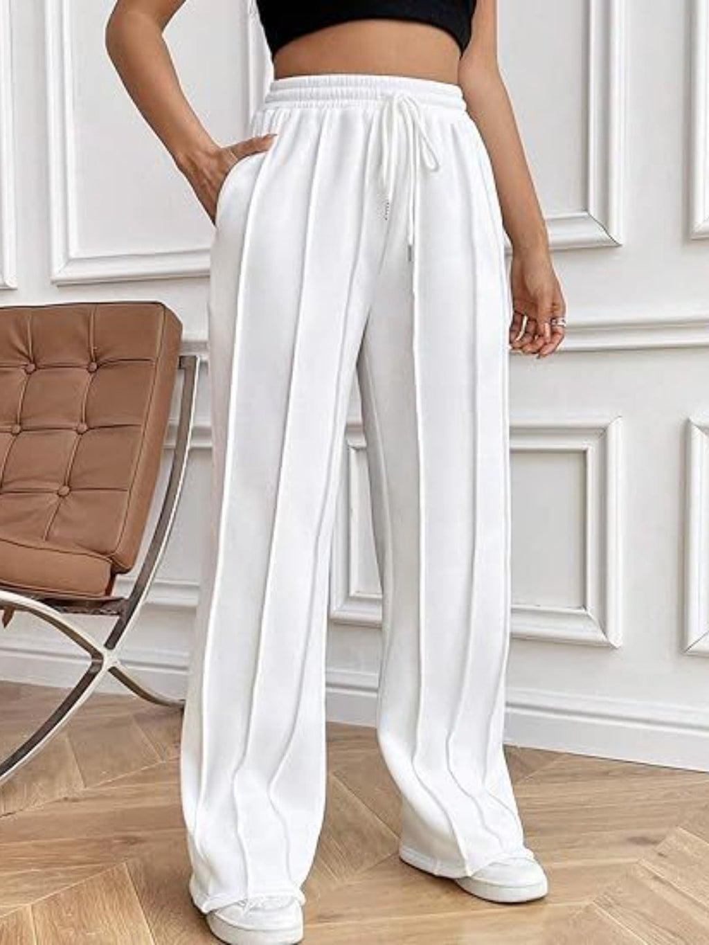 Model wearing high-waisted white wide leg drawstring pants with side pockets and vertical seam details.