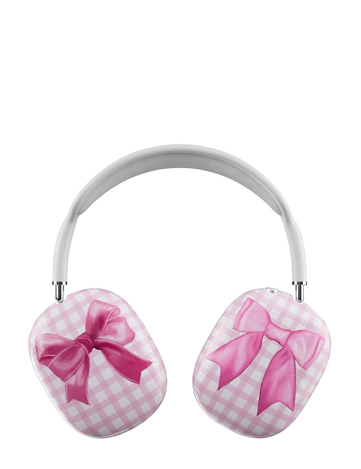AirPods Max headphones wearing a protective cover with a pink gingham pattern and large pink bows on each side.