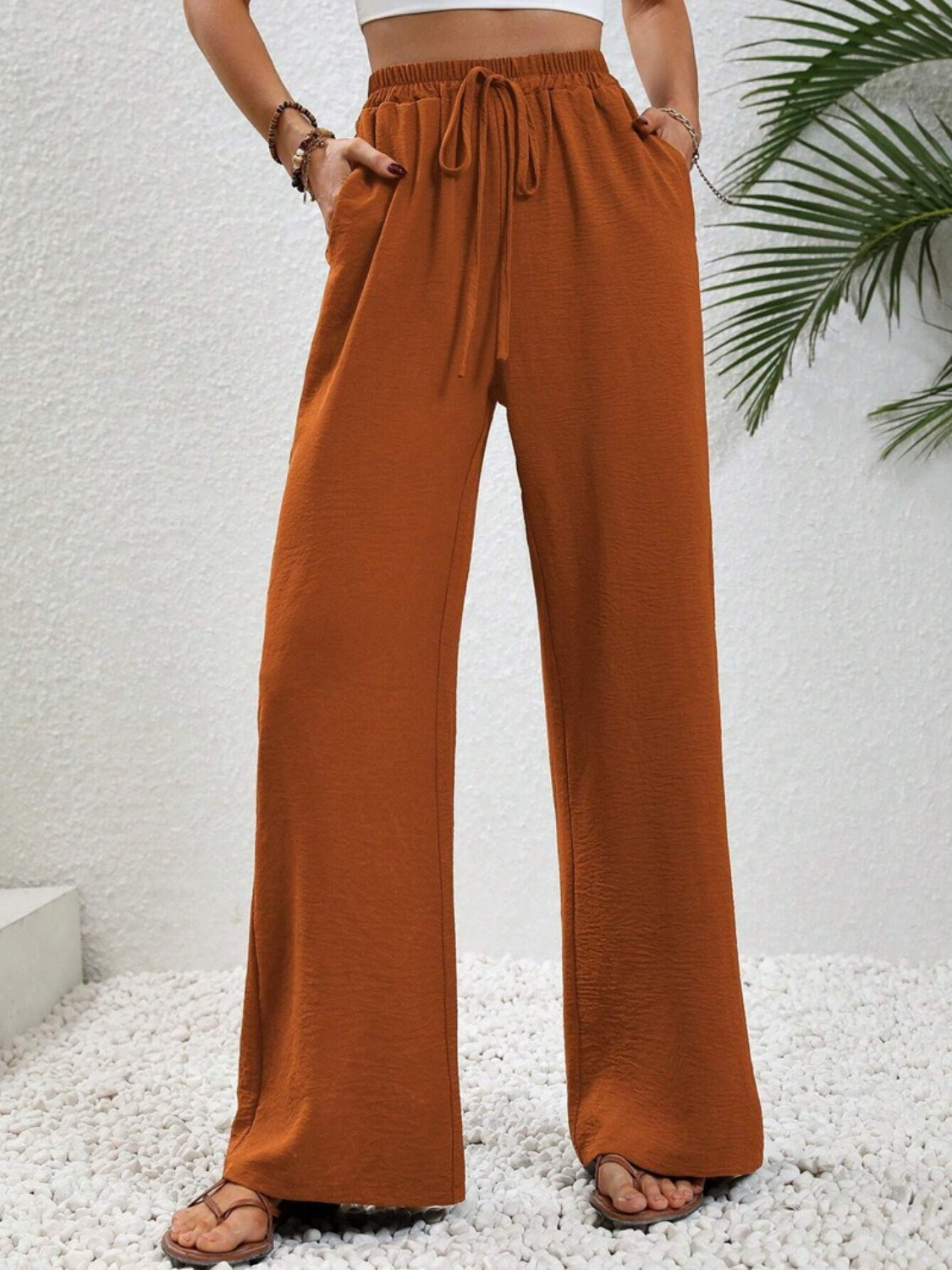 A woman wearing rust-colored wide-leg drawstring pants paired with a crop top, shown in front and back views.