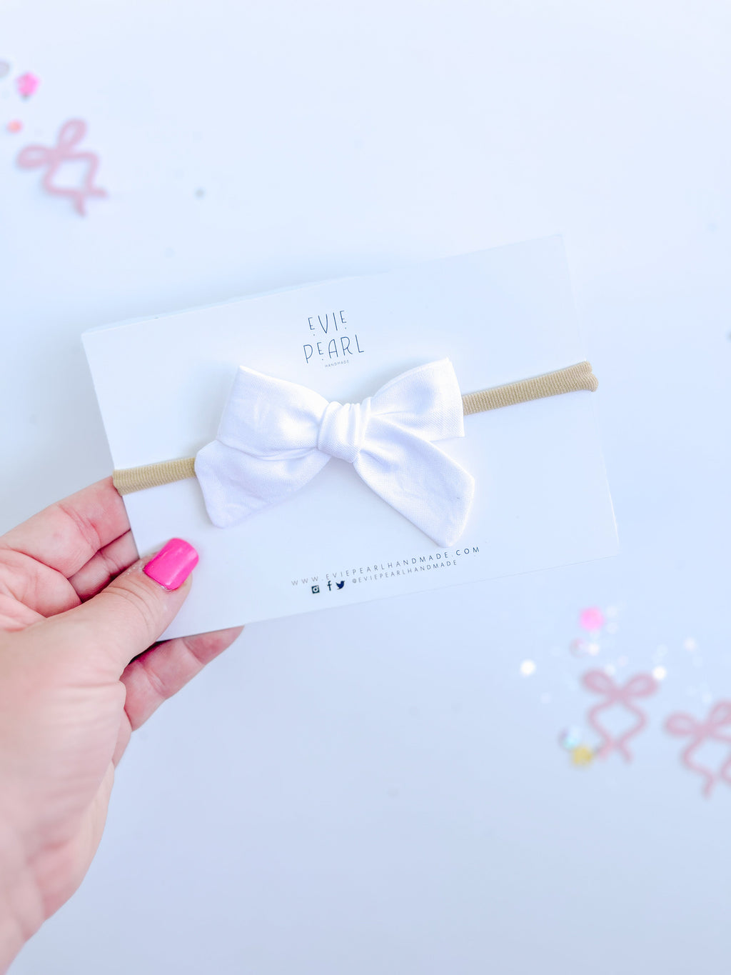 A white cotton mini pinwheel bow attached to a tan headband, displayed on a branded Evie Pearl Handmade backing card.