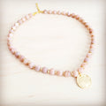 Frosted sunstone beaded collar necklace with a central matte gold-tone pendant on a light wood background