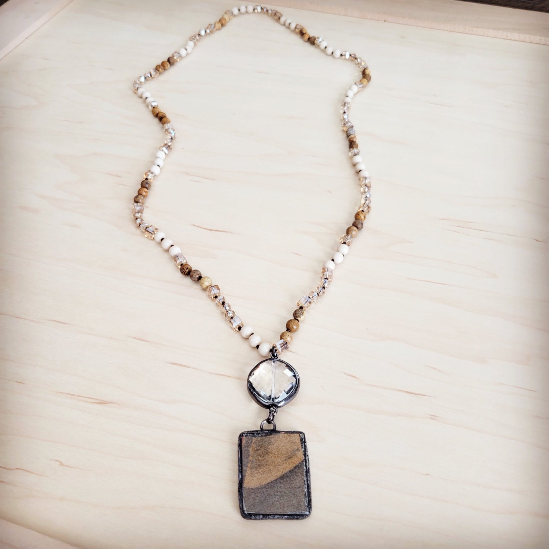 Long necklace featuring beige and brown Picture Jasper beads, clear crystal spacers, a faceted clear crystal accent, and a rectangular Jasper pendant in a dark metal setting.