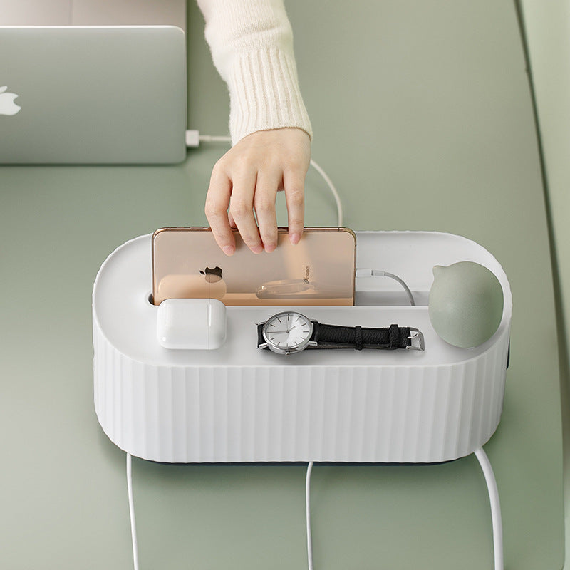 Minimalist navy blue cable management storage box on a desk holding a power strip and mobile phone.