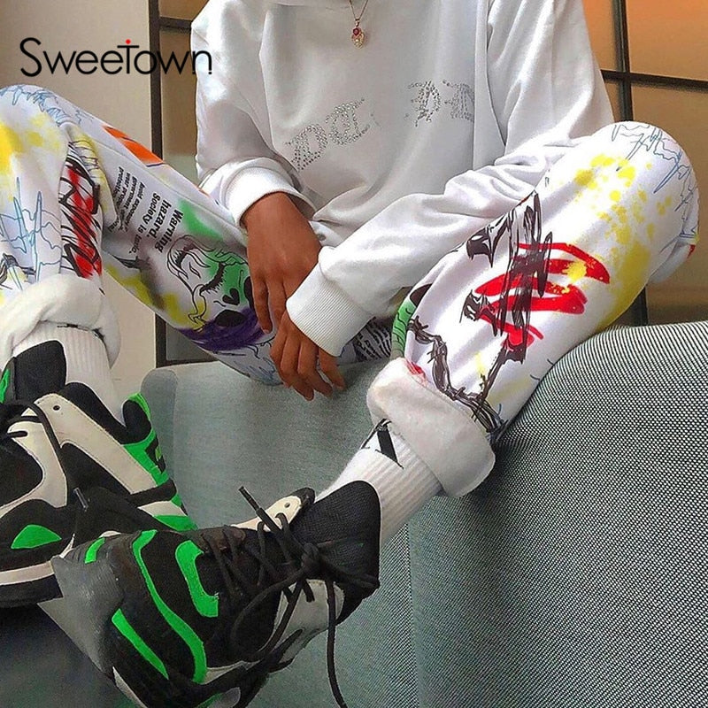 A female model wearing Sweetown Harajuku graffiti print baggy cargo jogger pants with a white top and sneakers, showcasing the vibrant design and relaxed fit.