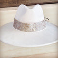 A close-up view of a wide, embossed, and gilded genuine leather cowboy hat band on a white felt hat.