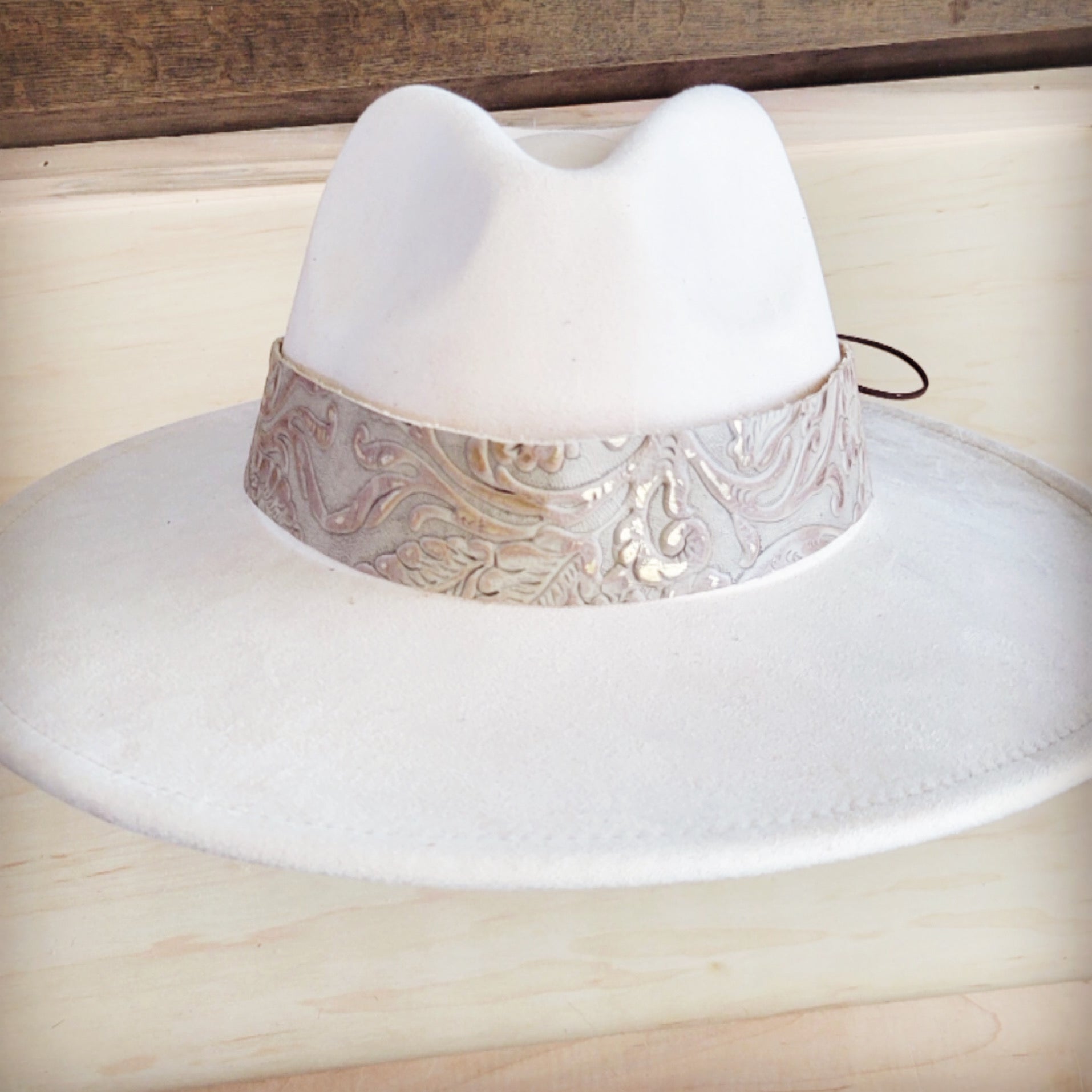 A close-up view of a wide, embossed, and gilded genuine leather cowboy hat band on a white felt hat.