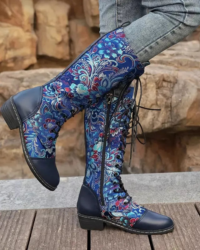 Blue floral-patterned boots worn with gray pants against a stone wall background