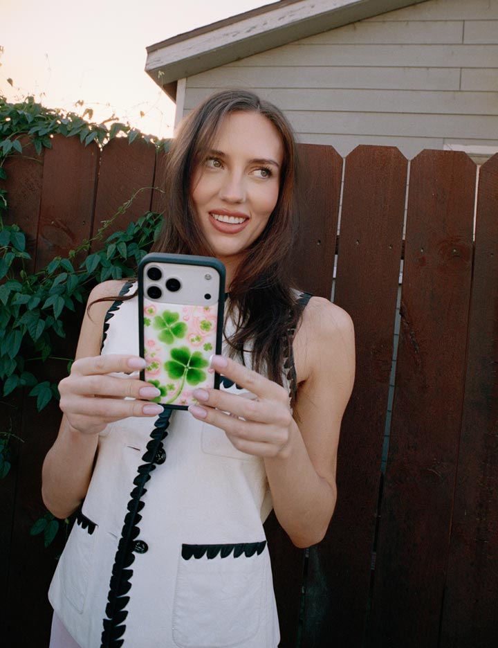 Woman holding a phone with a floral case in front of a wooden fence