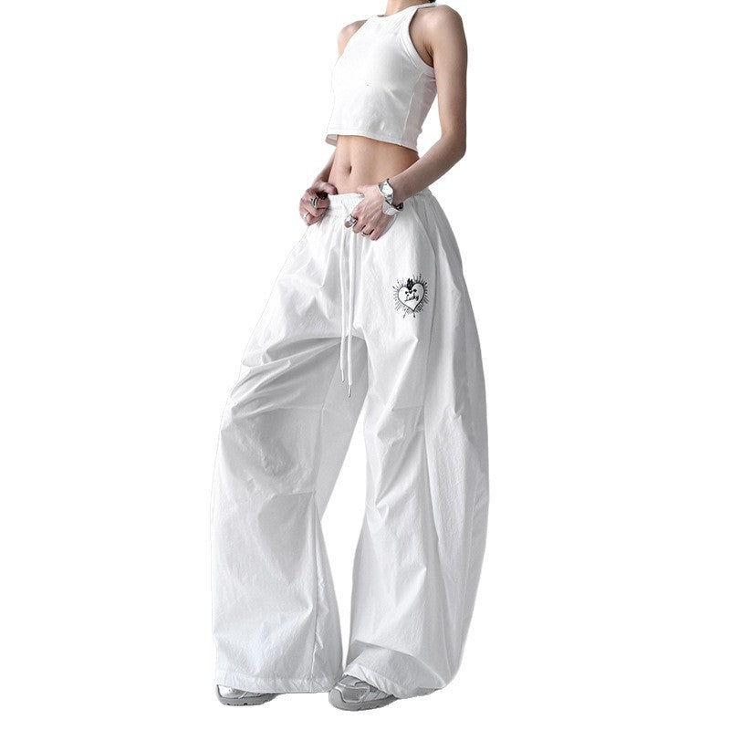 A female model wearing Harajuku Style Quick Drying Wide Leg Sports Pants in white, featuring a drawstring waist and a subtle heart graphic. Another image shows the black version of the pants.
