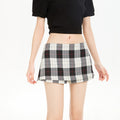 A model wears a black and white plaid A-line mini skirt with red accent lines, paired with a black crop top and white knee-high socks.