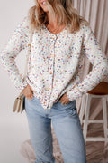 A woman wearing a white button-front cardigan sweater with a multicolor confetti pattern and rhinestone embellishments, styled with light wash jeans.