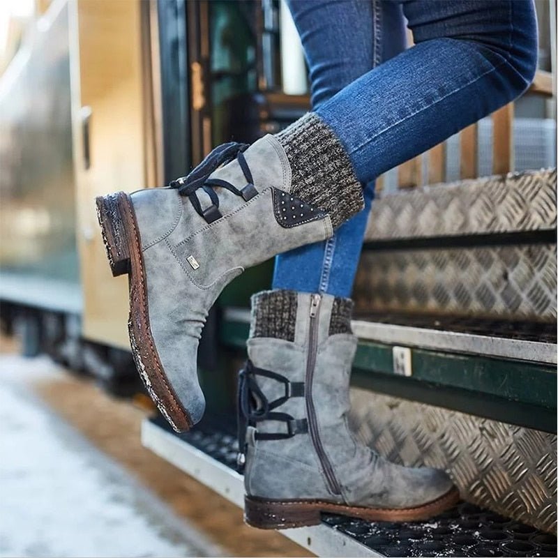 A woman wearing grey mid-calf flocked suede winter boots with a knitted cuff and blue jeans, standing on snowy stairs.