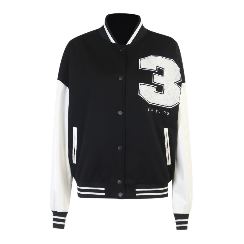 Women's black and white varsity baseball jacket with a large '3' and 'EST. 76' graphic, shown on a model embracing a casual, trendy street style.
