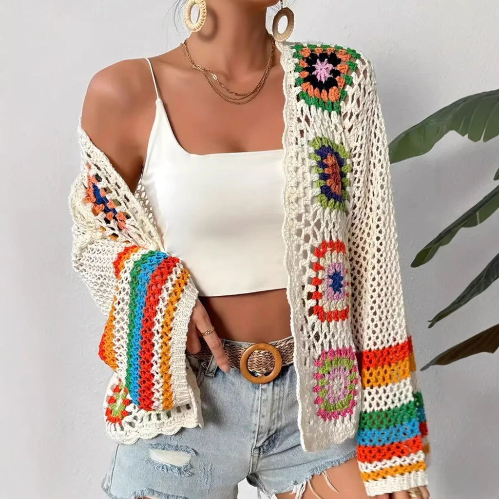 Model wearing a hand-crocheted geometric knit cardigan with multi-colored accents over a white tank top and denim shorts.