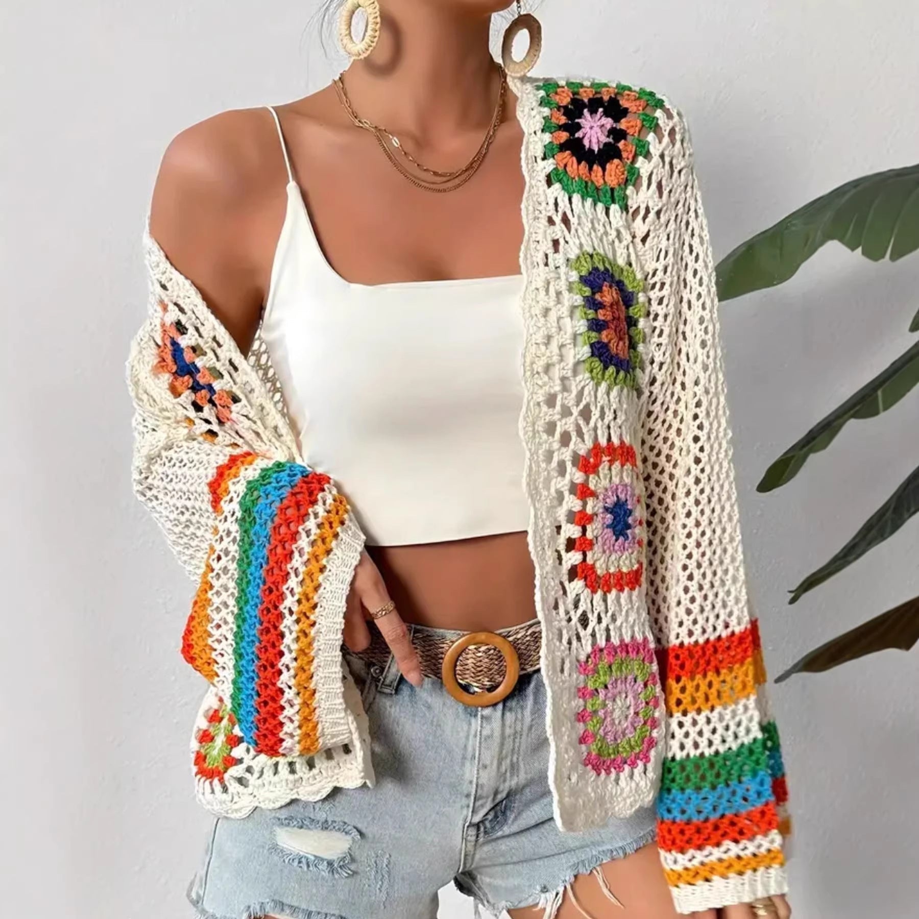 Model wearing a hand-crocheted geometric knit cardigan with multi-colored accents over a white tank top and denim shorts.