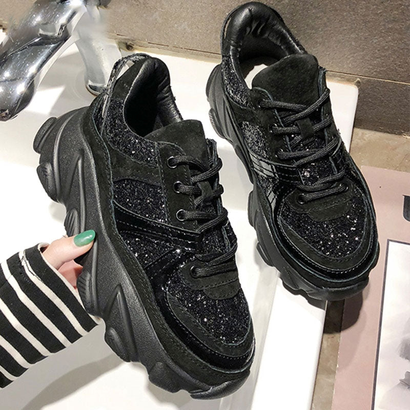 A pair of black chunky platform wedge sneakers with glitter accents displayed in a high-fashion Harajuku style.