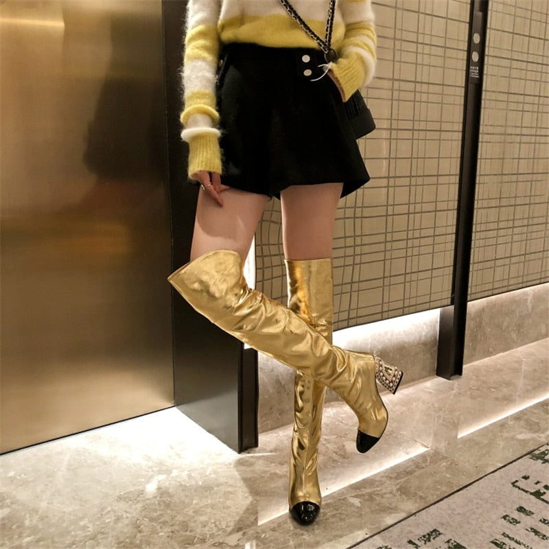 Fashionable women's over-the-knee boots in gold and white with a pointed black toe and unique sculpted, pearl-patterned heel, perfect for statement style.