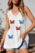 A woman wearing a white waffle knit tank top featuring several colorful sequin butterfly patches against a light grey background.