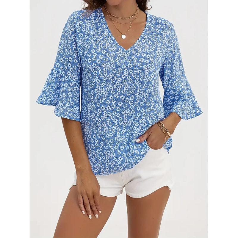 A woman wearing a blue floral V-neck blouse with flared sleeves tucked into white shorts