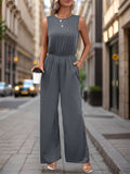 A woman wearing a charcoal grey sleeveless wide leg jumpsuit with pockets standing on a city street.