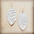 A pair of white leather oval earrings with a gold-tone gator print pattern and gold-tone fish hooks resting on a wood background.
