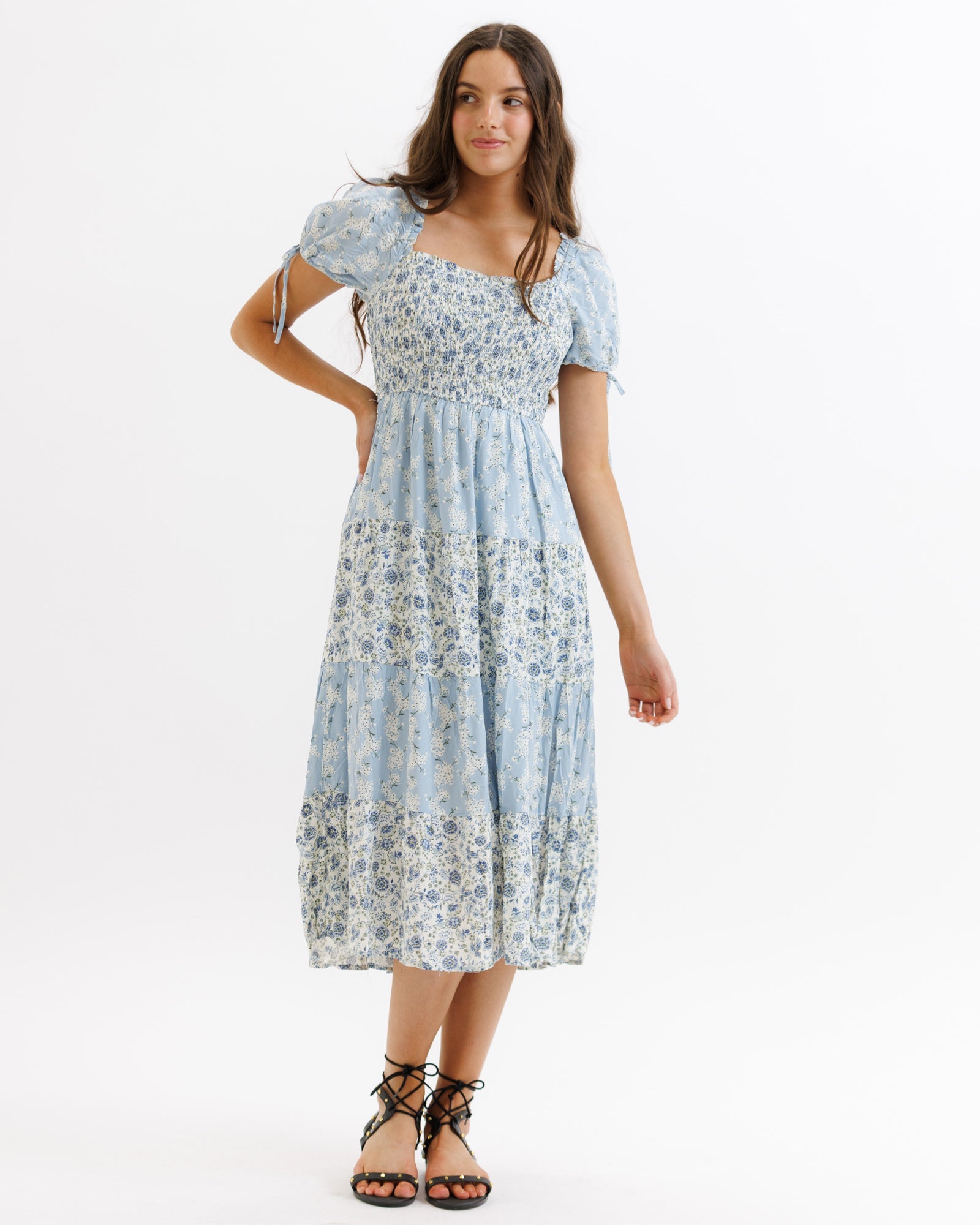 Front and back view of a woman wearing a blue floral midi dress with a square neckline, puffed sleeves, and smocked bodice.