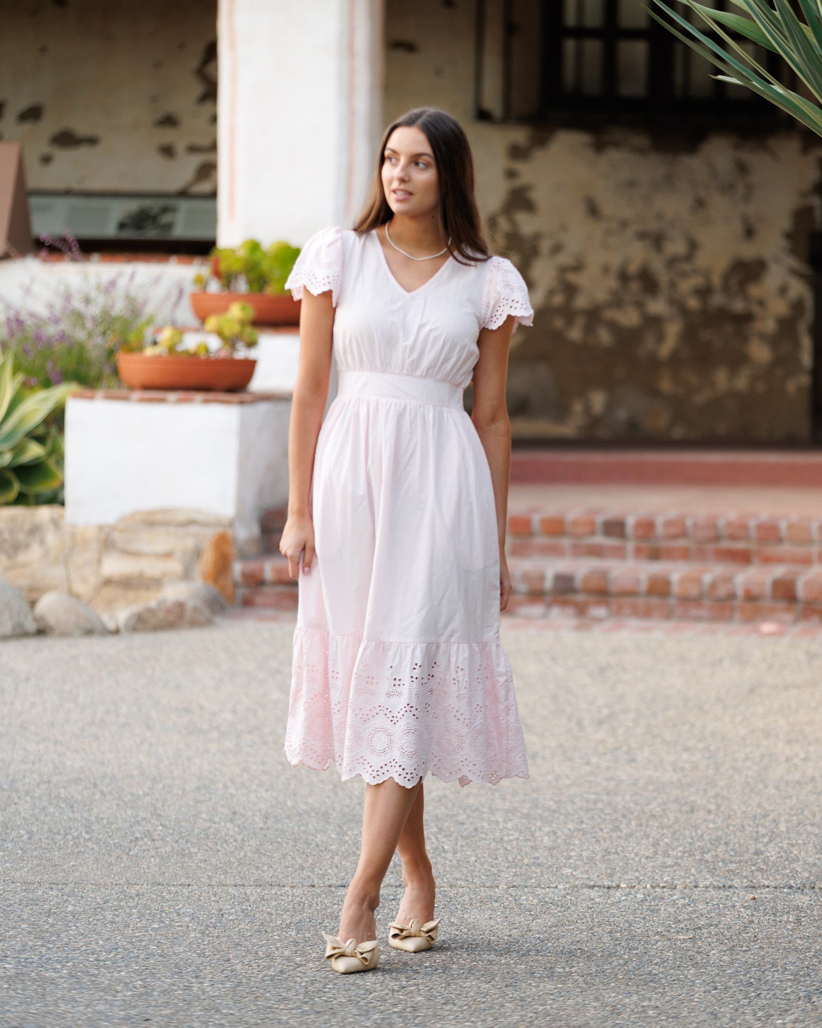 A woman wearing a pink midi-length eyelet dress with flutter sleeves and a V-neckline.