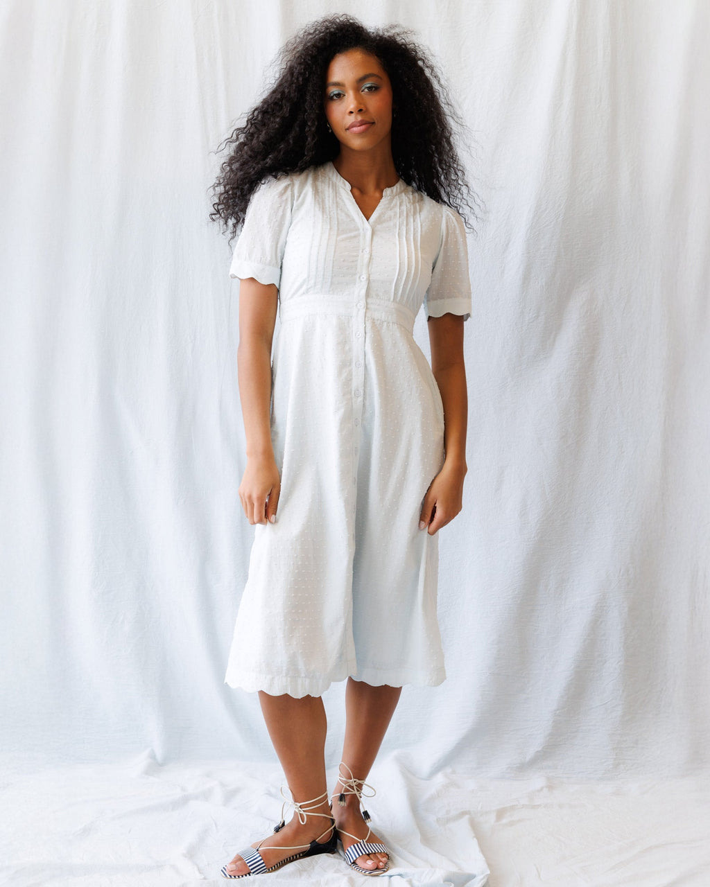 Woman wearing a Swiss dot midi dress with puff sleeves and pintuck detailing in white