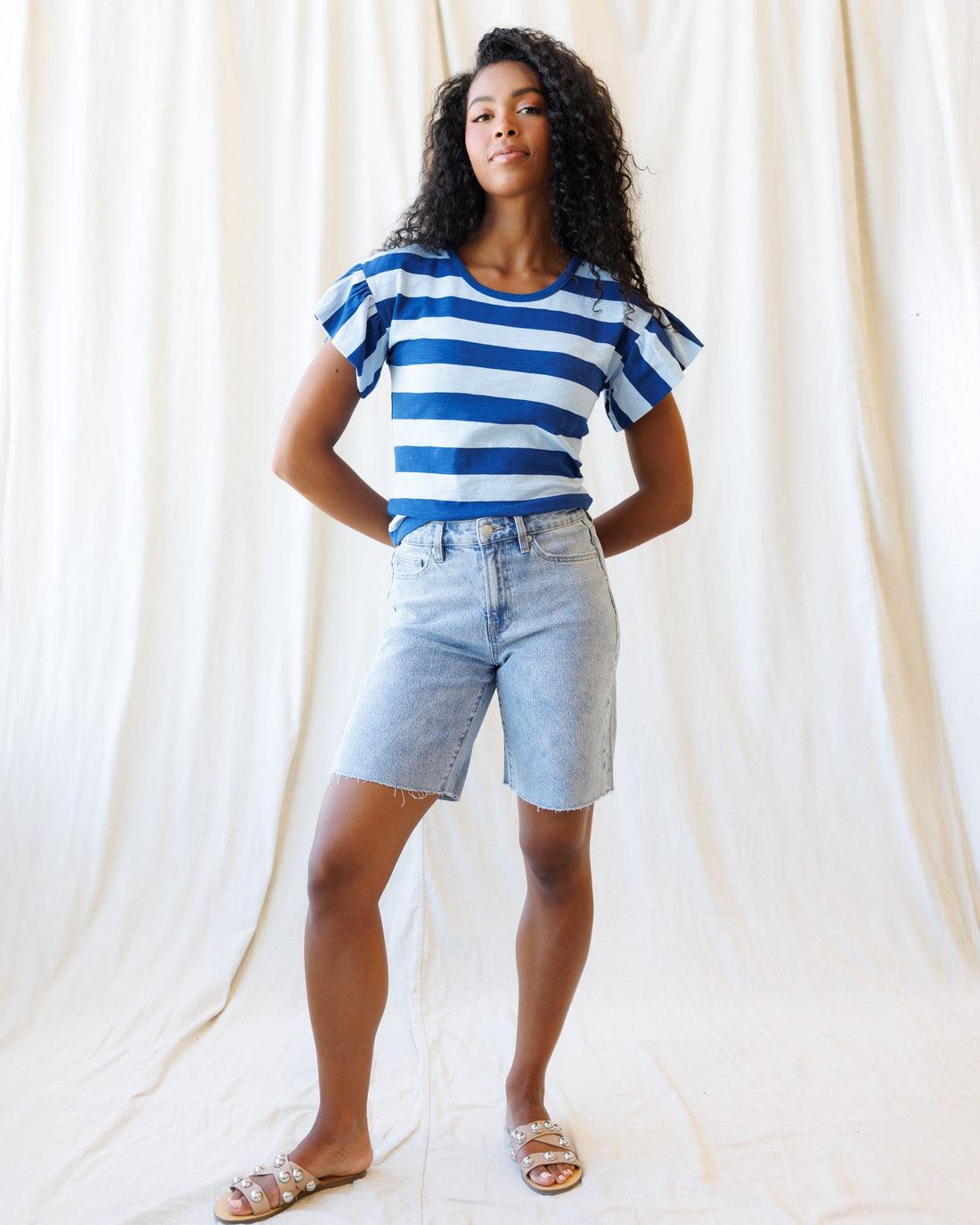 A pair of high-rise, light-blue denim shorts with a raw hem and relaxed fit, shown against a neutral background.