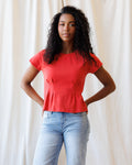 Close up of a red cotton short sleeve tee featuring a V-stitch neckline and subtle waist pleats