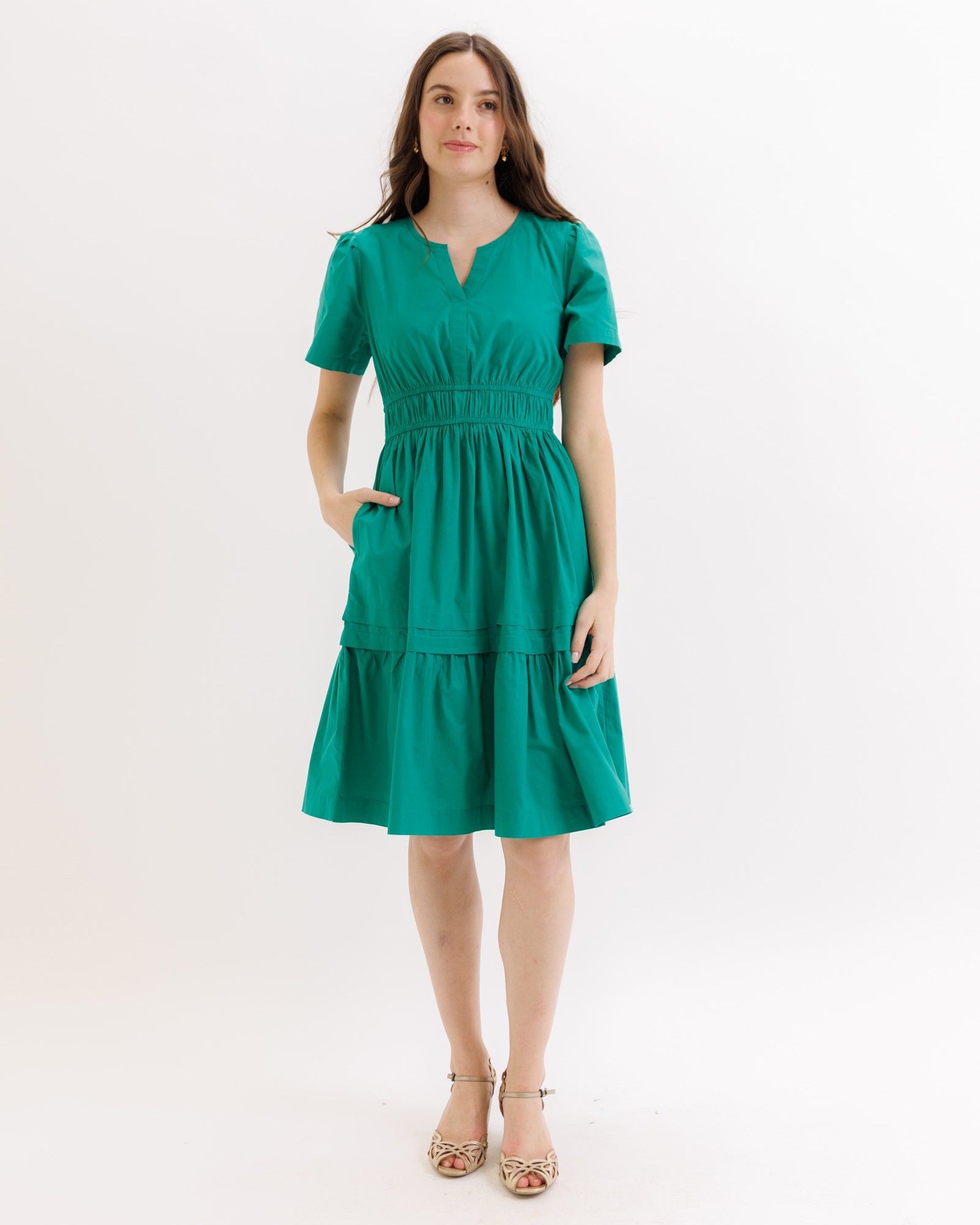A woman wearing a knee-length green cotton tiered dress with a split neckline and pockets.