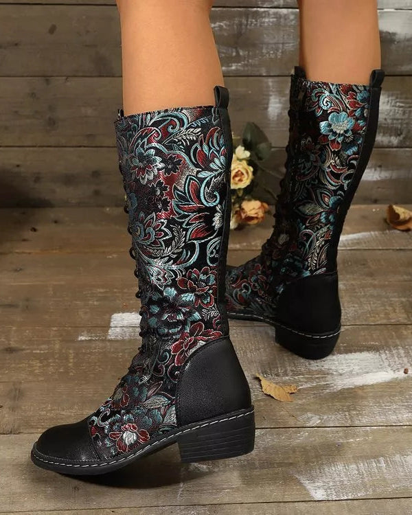 Decorative knee-high boots with floral patterns on a wooden floor.