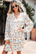 Model wearing a white mini dress with yellow and green floral print, long sleeves, and tie neck detail