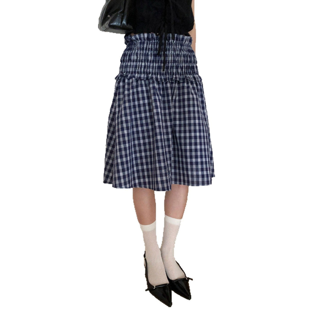 Model wearing a blue and white plaid smocked waist midi skirt with a black top and black shoes.