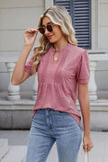 A woman wearing a pink notched neck short sleeve top with vertical pleats, paired with blue jeans.