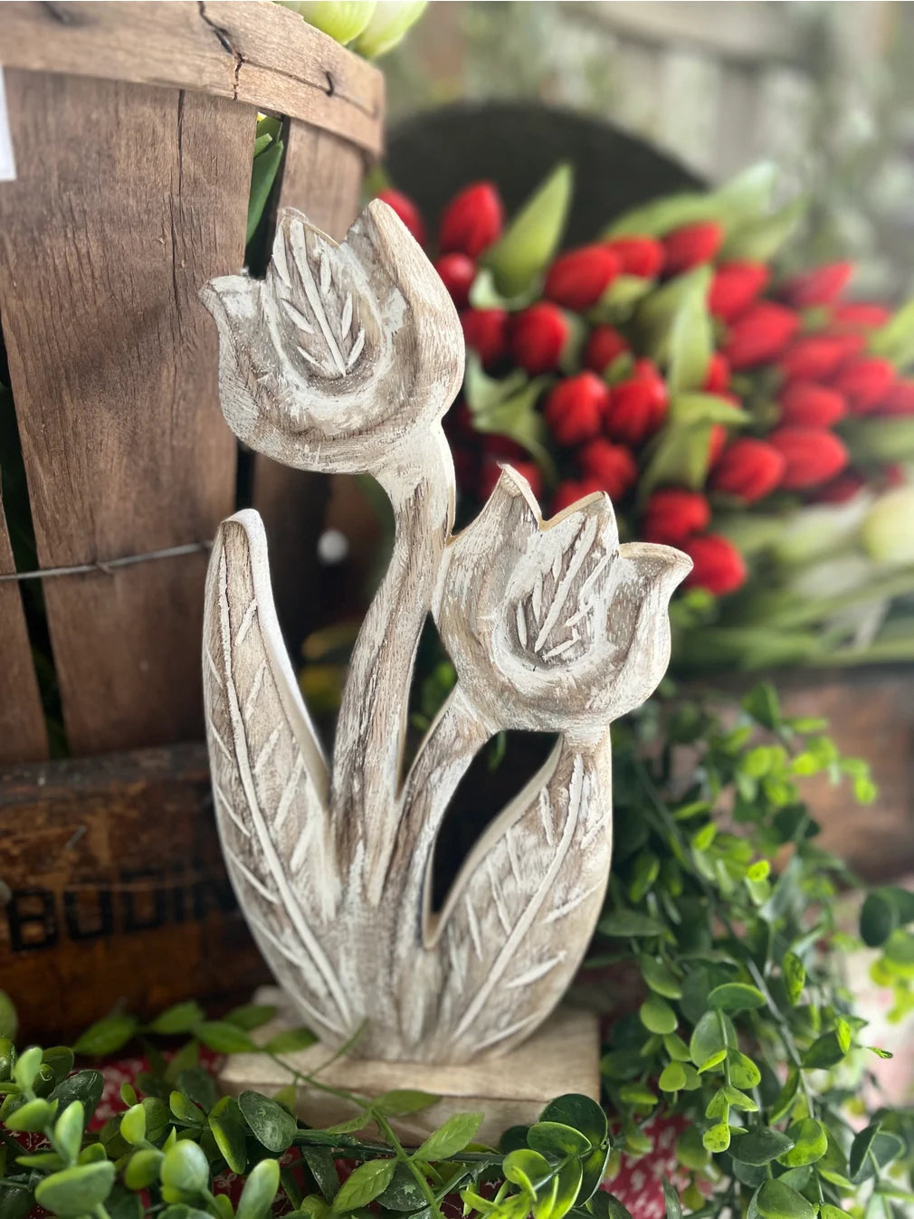 A decorative whitewashed wooden tulip figurine displayed on a rustic background.