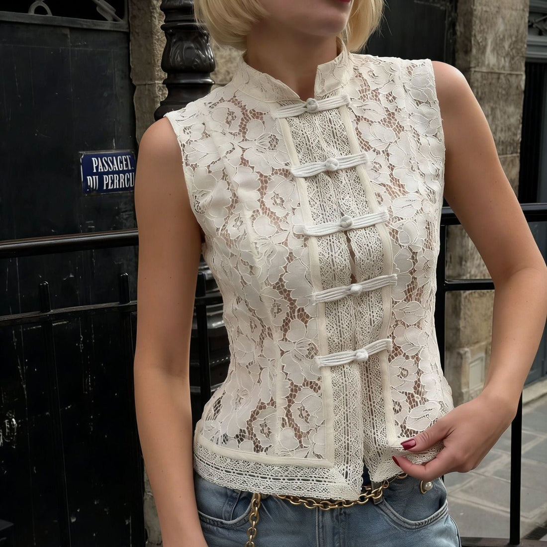 Woman wearing a cream-colored floral lace sleeveless top with a mandarin collar and knot buttons