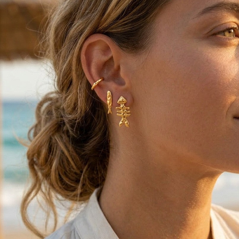 A pair of polished 18K gold plated stainless steel fishbone stud earrings on a white background