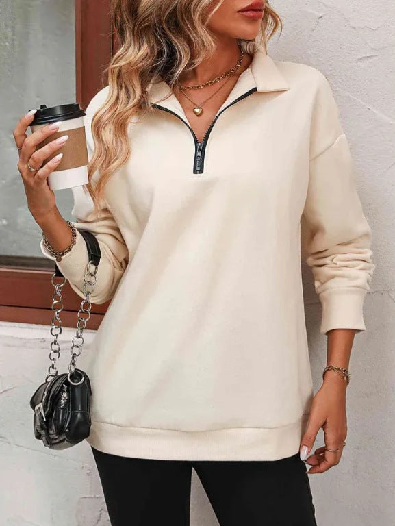 Woman wearing a beige pullover with a zipper, holding a coffee cup and a black handbag.