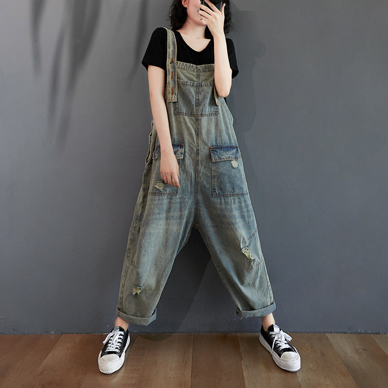 A woman wearing baggy retro-style light wash ripped denim overalls with a black t-shirt and sneakers