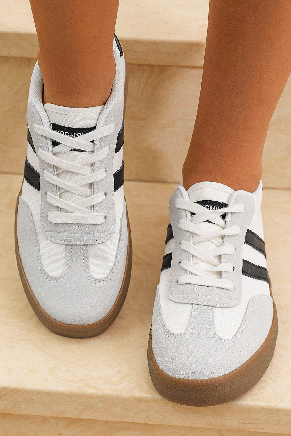 Close up view of white lace up sneakers with black side stripes and gum rubber soles on a person