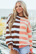 A woman wearing a brown, white, and peach color-blocked striped pullover sweatshirt with drop shoulders.