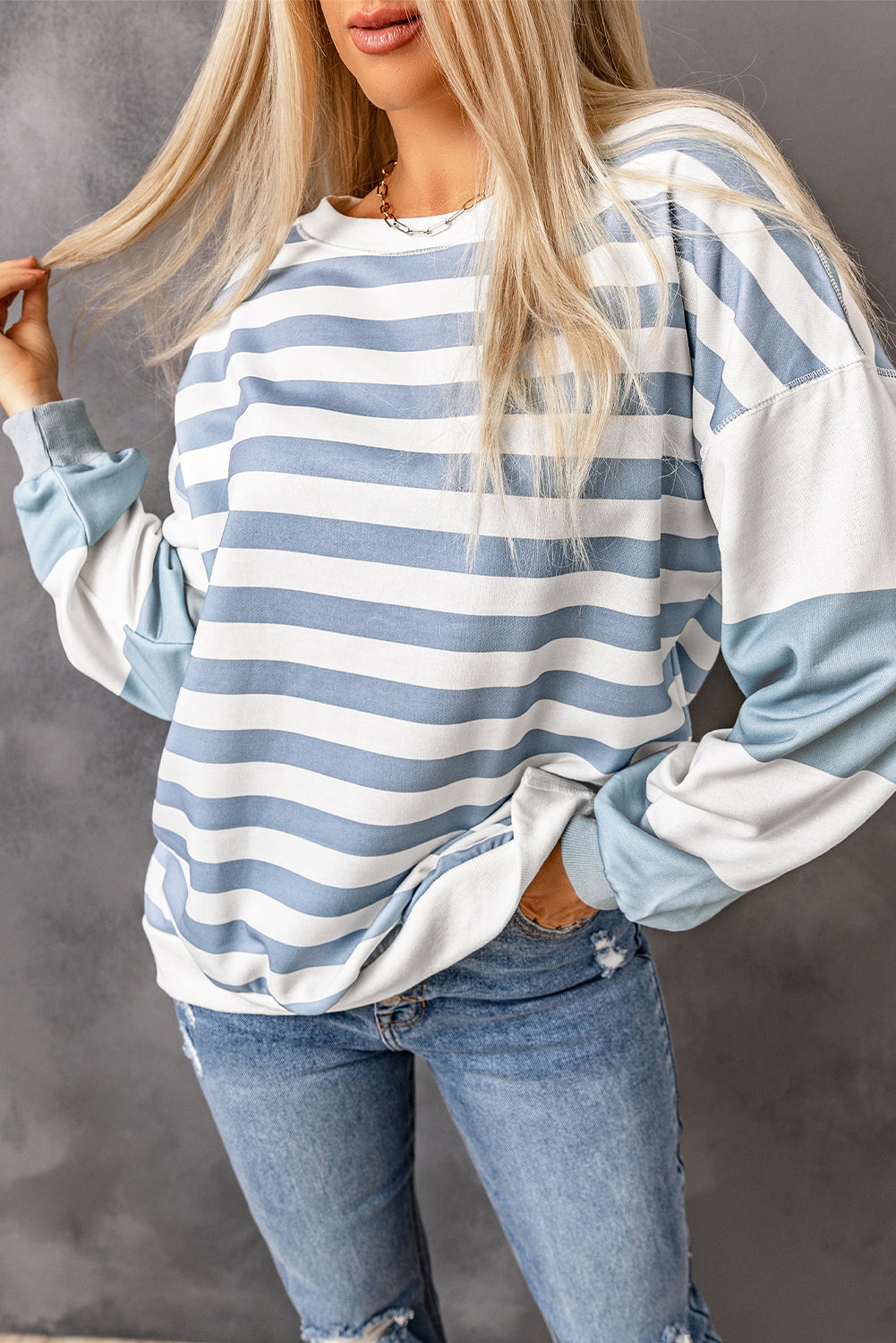 Model wearing a blue and white striped crew neck sweatshirt with colorblock sleeves and side slits.