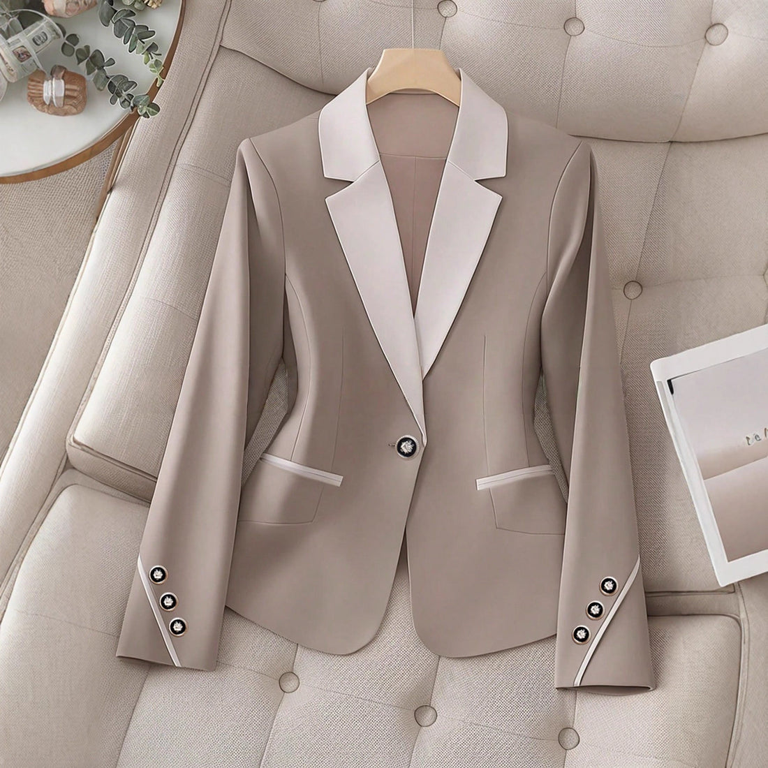 A beige and white contrasting color blazer with a single button closure displayed on a tufted chair.