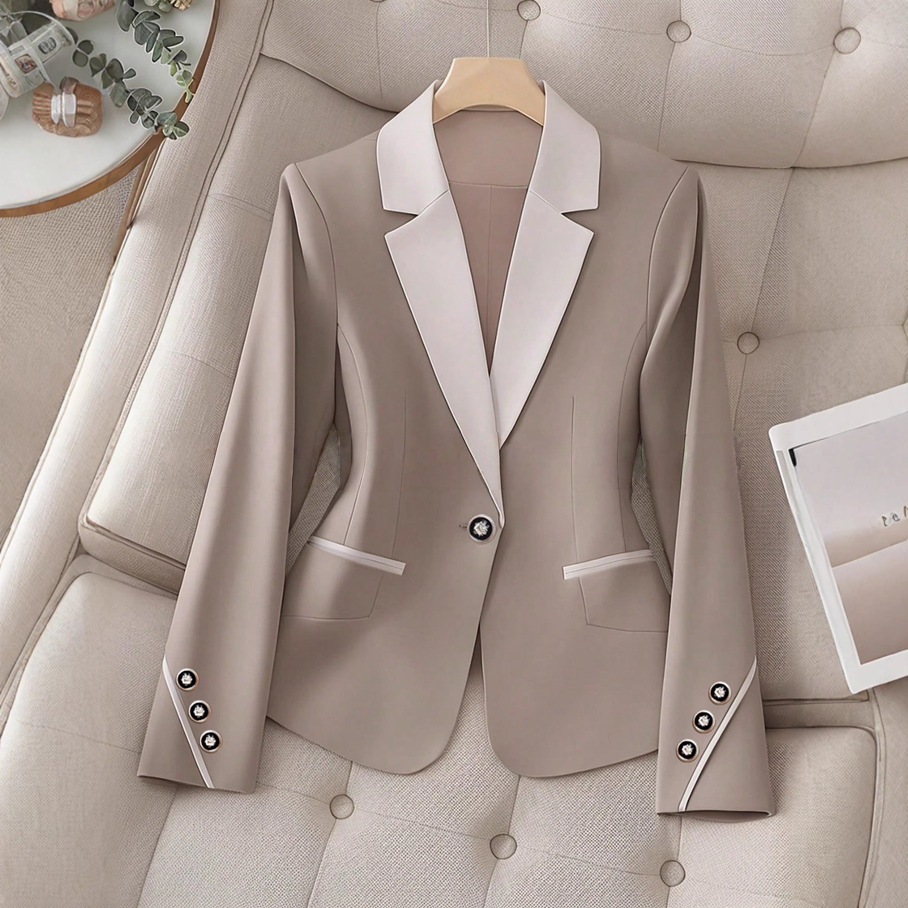 A beige and white contrasting color blazer with a single button closure displayed on a tufted chair.