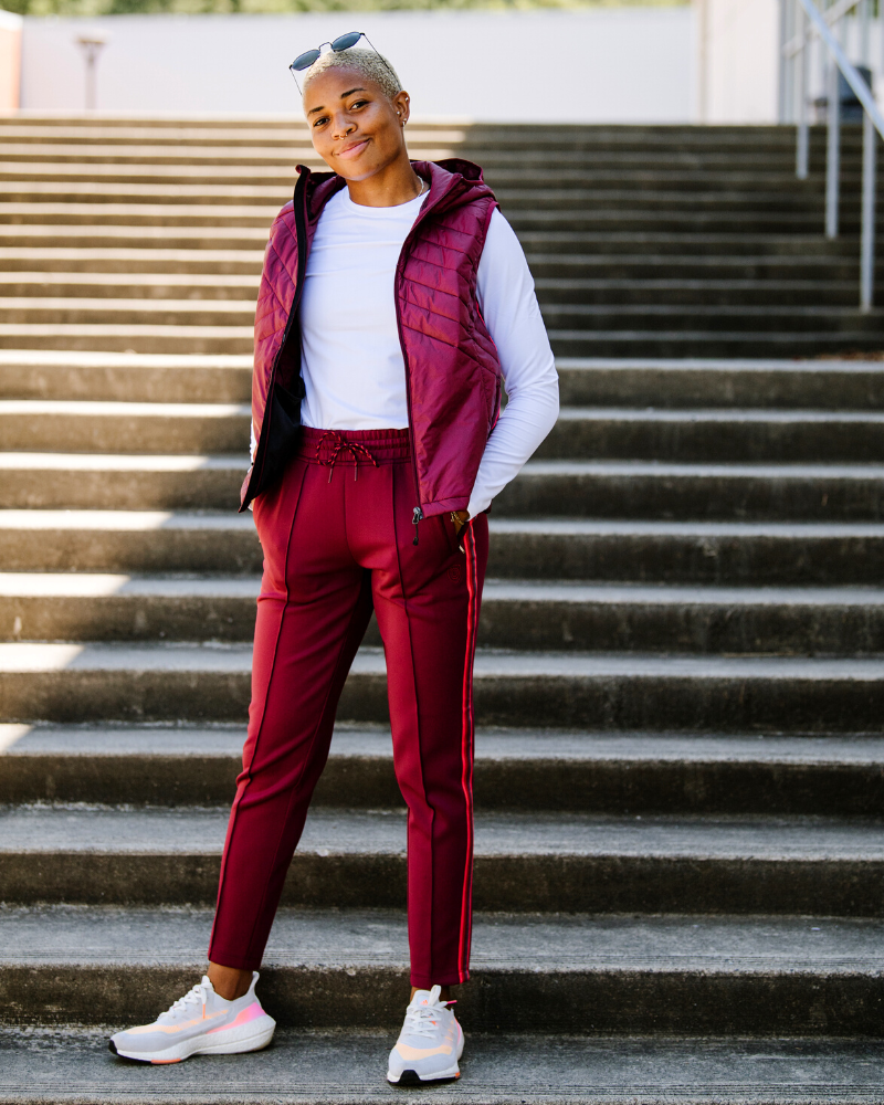 A person wearing burgundy mid-rise track pants with a stripe detail down the leg, paired with a matching jacket.