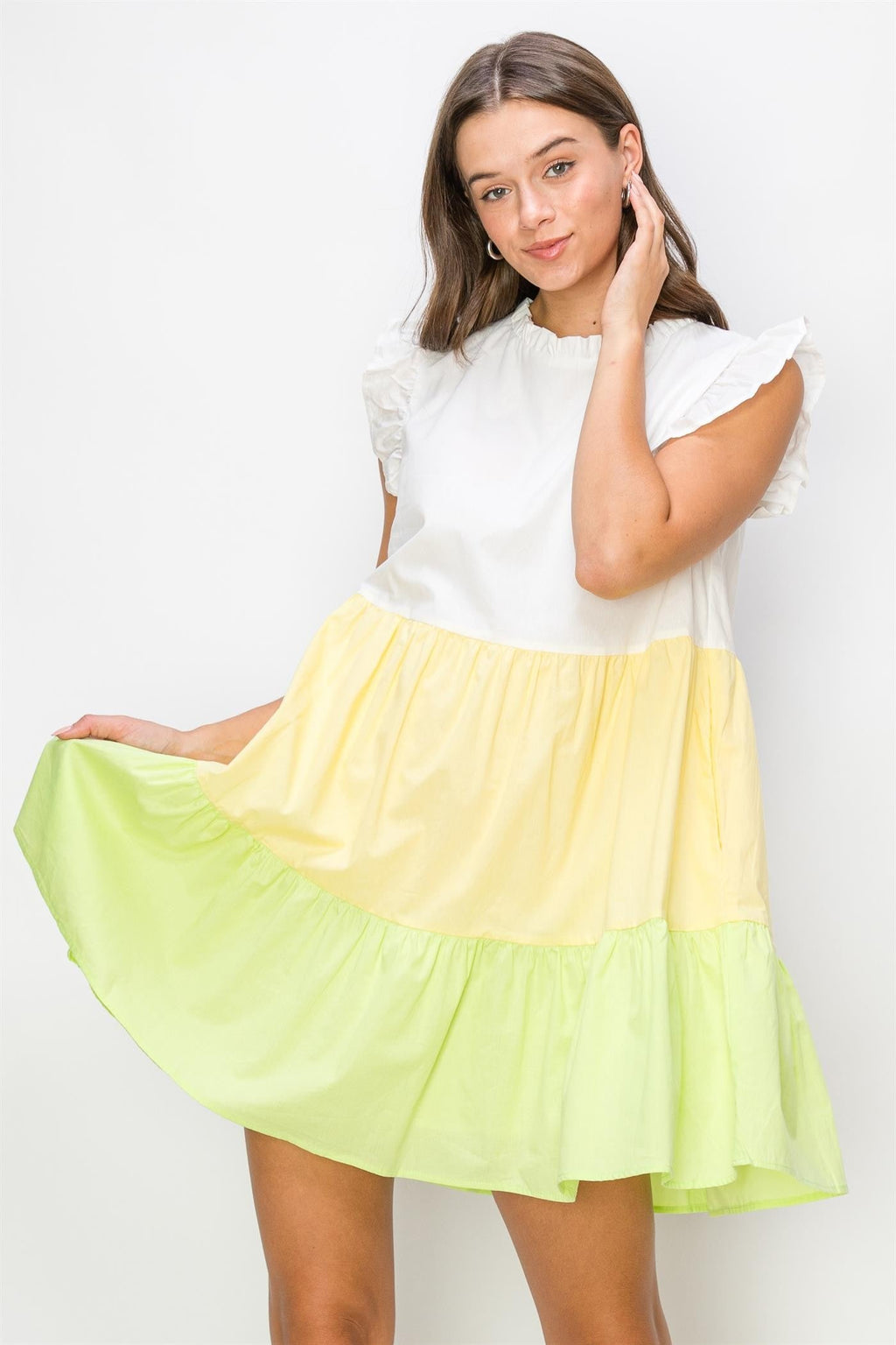 A woman wearing a white, yellow, and lime color-blocked poplin mini dress with tiered hem and ruffle sleeves against a white background.